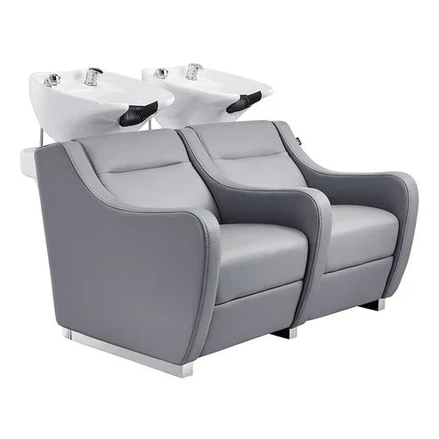 A sleek double gray leather salon shampoo backwash unit with an adjustable white ceramic tilting bowl and chrome fixtures.