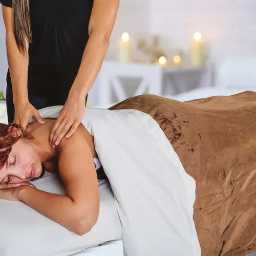 A professional massage table neatly made with high-quality white cotton linens and a plush, ultra-soft fleece face cradle cover.