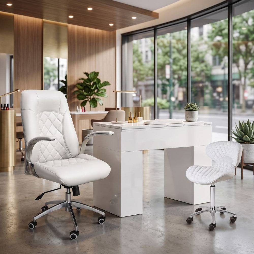 White quilted ergonomic nail tech chair and technician stool at a modern white manicurist desk in a salon.