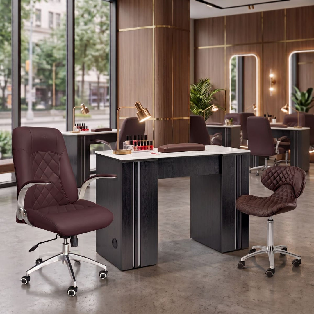 Luxury nail salon manicure station with dark wood desk, burgundy quilted leather chair, and manicurist stool.