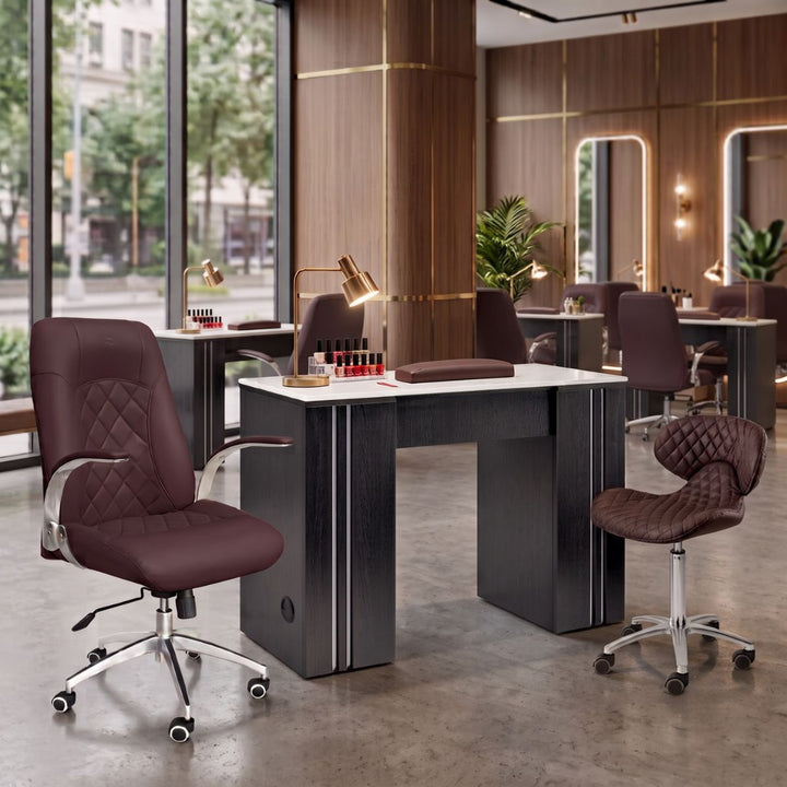 Luxury nail salon manicure station with dark wood desk, burgundy quilted leather chair, and manicurist stool.