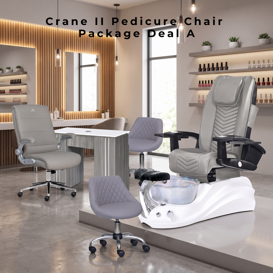 Promotional image for the "Crane II Pedicure Chair Package Deal A" set inside a modern nail salon. In the foreground, a large grey pedicure chair is mounted on a wavy white base with a glass foot basin, accompanied by a small, matching grey quilted technician stool. To the left, a grey upholstered salon chair sits in front of a light wood-paneled manicure table. The background features warm vertical wood paneling, mirrors, shelving stocked with nail polish bottles, and soft pendant lighting.