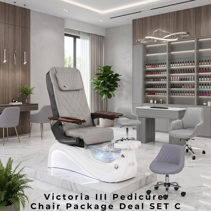 Victoria III Pedicure Chair Package Deal SET C featuring a luxury grey leather pedicure chair with a white base and glass basin, a grey wood-grain manicure table with matching diamond-stitched client chairs, and a rolling technician stool in a contemporary salon interior with a large polish display wall.
