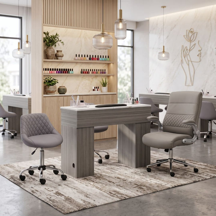 Modern grey manicure table station set with ergonomic technician and client chairs in a luxury nail salon setting.